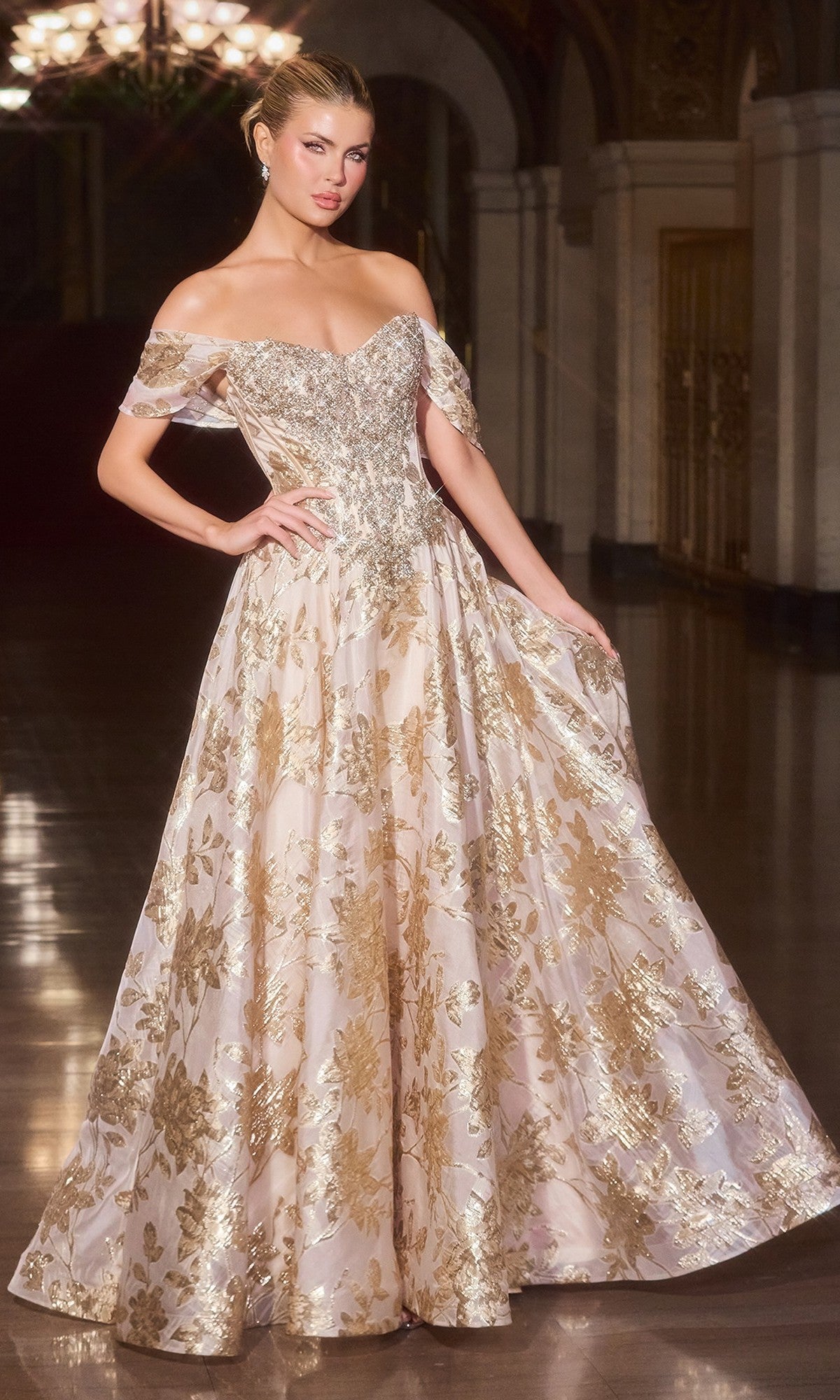 A woman stands in an ornate, dimly lit hall wearing the Ladivine CD682 gold long prom dress, featuring an off-the-shoulder, floor-length silhouette with metallic floral jacquard.
